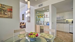 A modern kitchen with white cabinets, a microwave, and a glass dining table with a bowl of fruit.
