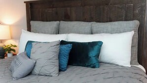 A bed with a grey quilt and multiple pillows in shades of grey, blue, and teal.