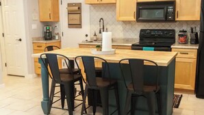 A kitchen with a central island, four chairs, wooden cabinets, a microwave, a stove, and a coffee maker.