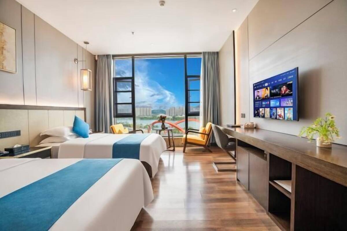 Habitación de hotel con dos camas, un escritorio, un televisor y un ventanal con vistas.