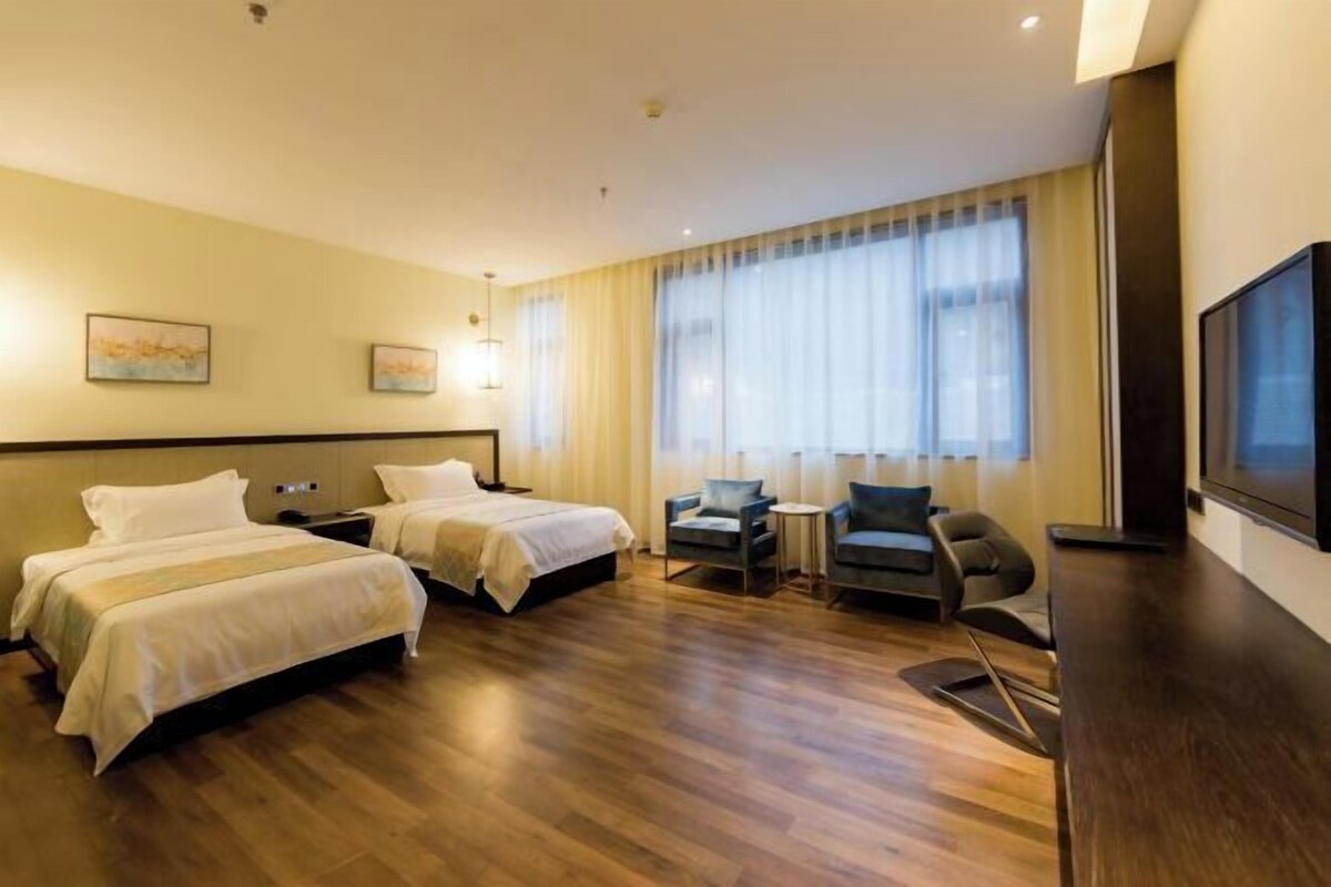 Una habitación de hotel con dos camas, un escritorio, una silla, un televisor y una ventana con cortinas.