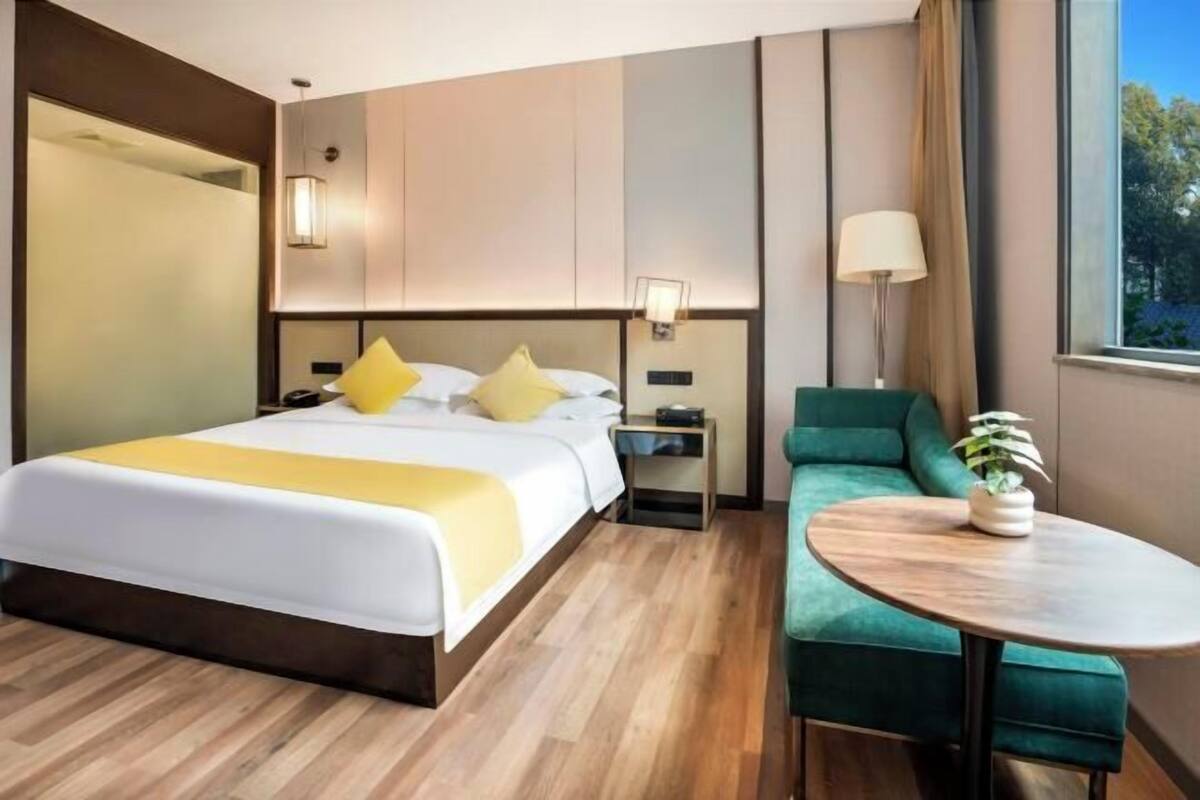 Una habitación de hotel con cama, mesita de noche, lámpara y una pequeña mesa redonda con una planta.