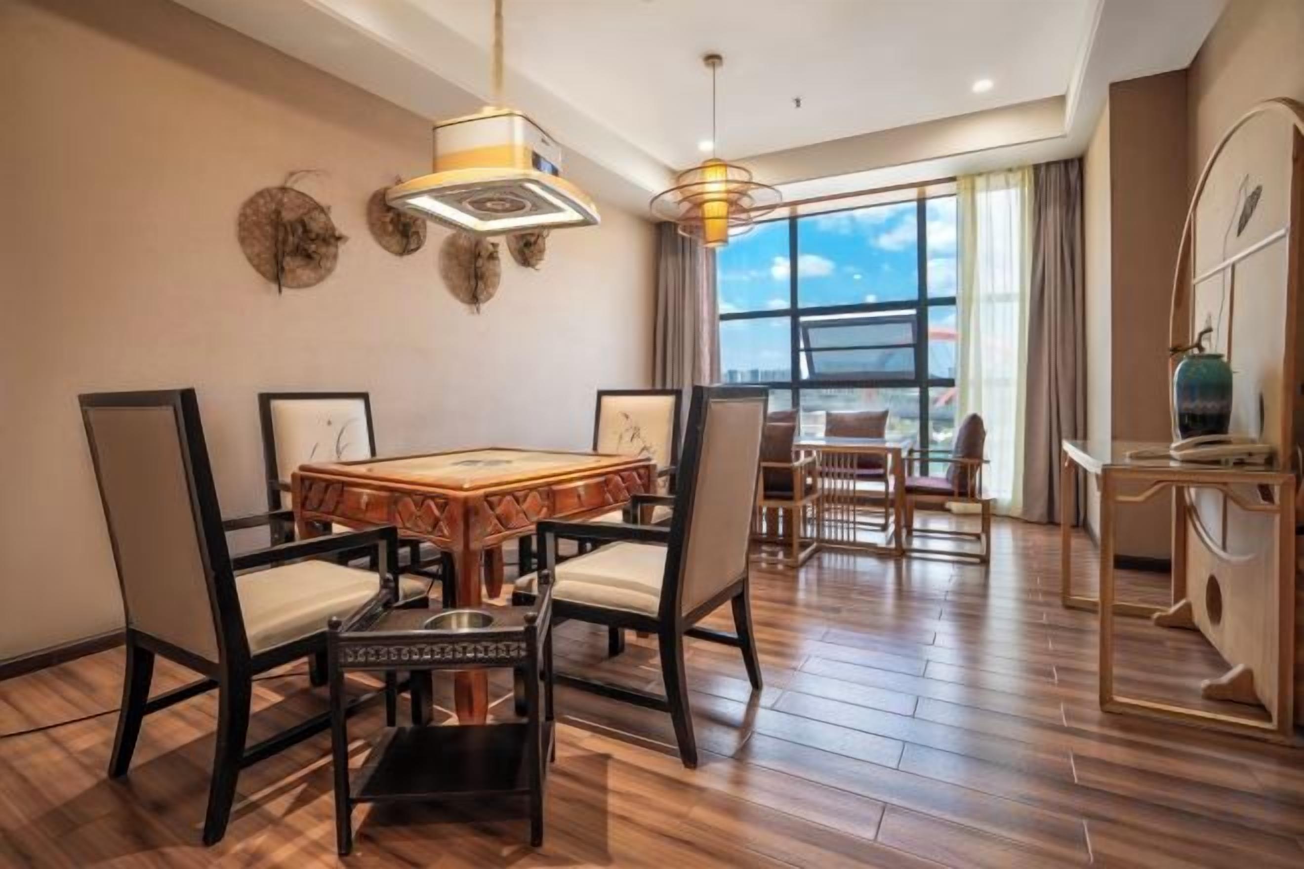 Un comedor con una mesa y sillas de madera, una lámpara de araña y vistas a través de ventanas amplias.