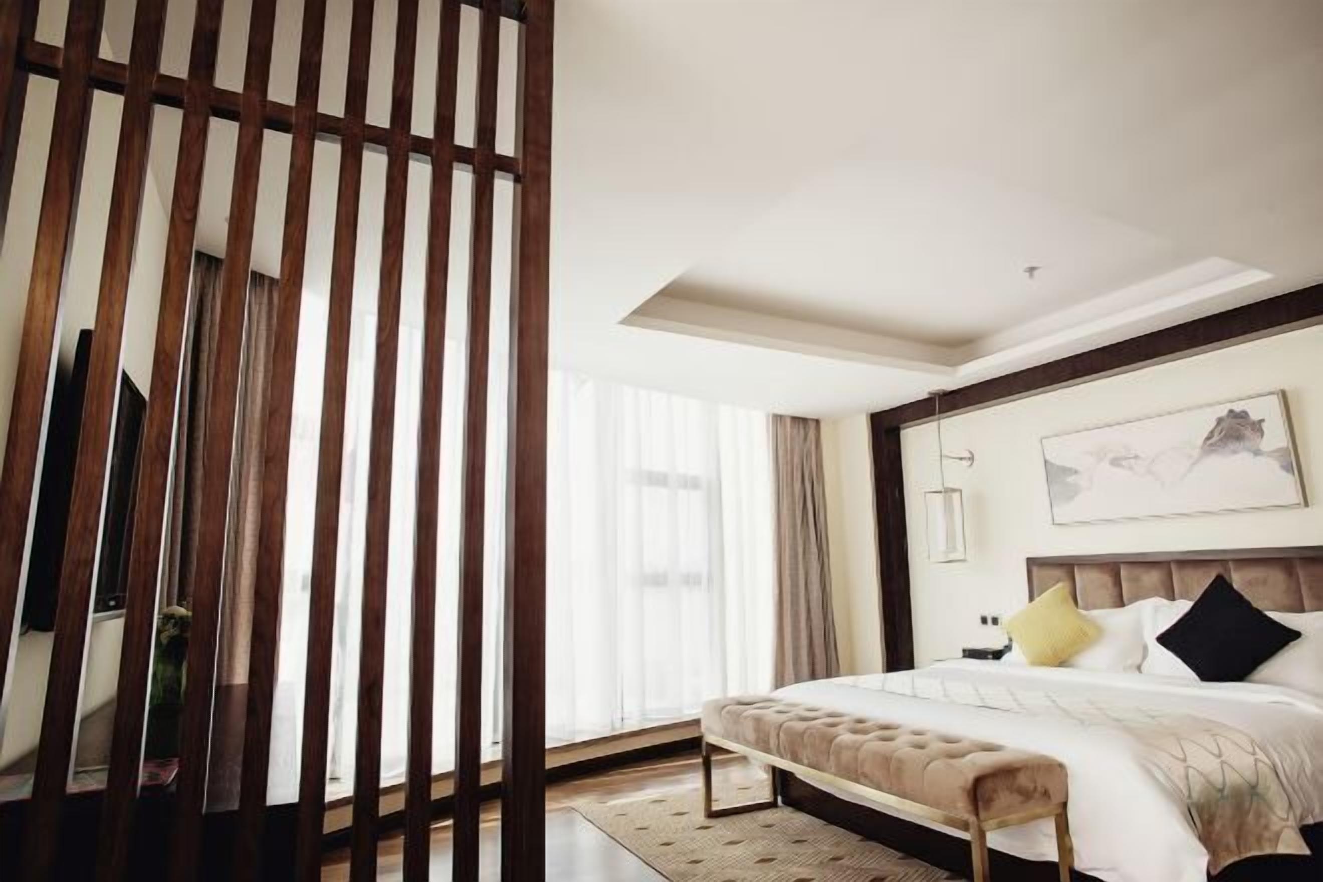 A modern hotel room with a large bed, a wooden partition, and a large window.