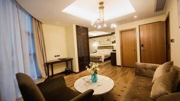 A hotel room with a sofa, a round coffee table with a vase, a bed, a desk, and a wardrobe.