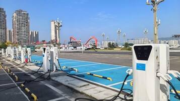 A parking area with electric vehicle charging stations, a clear sky, and distant buildings.