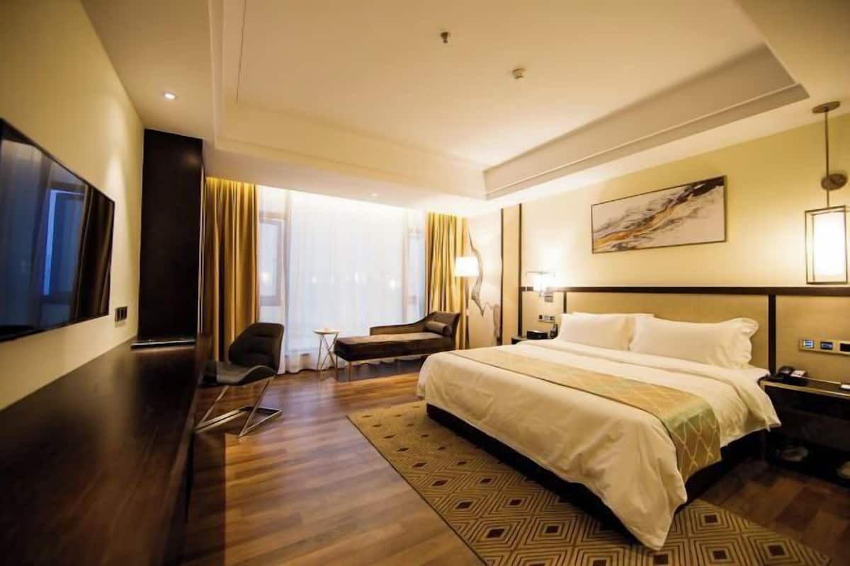 Una habitación de hotel con una cama grande, un escritorio, una silla, un televisor y una ventana con cortinas.