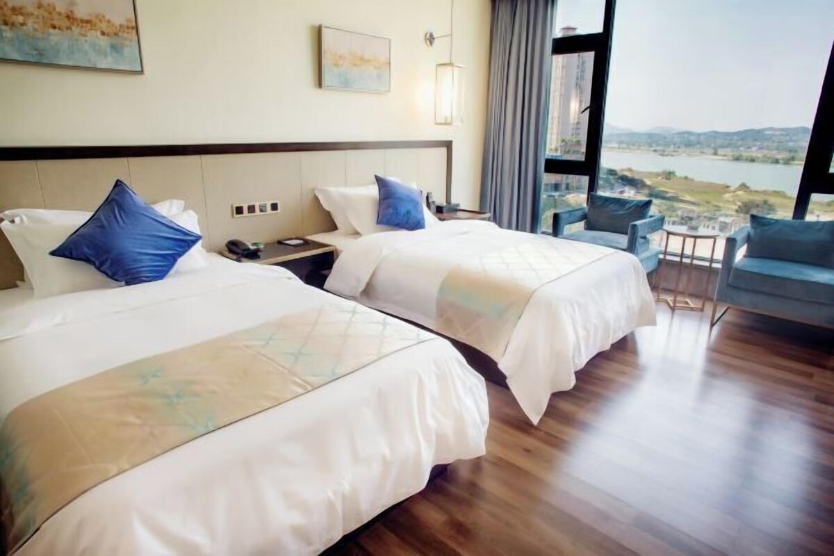 A hotel room with two beds, a nightstand, a chair, and a view of a body of water.