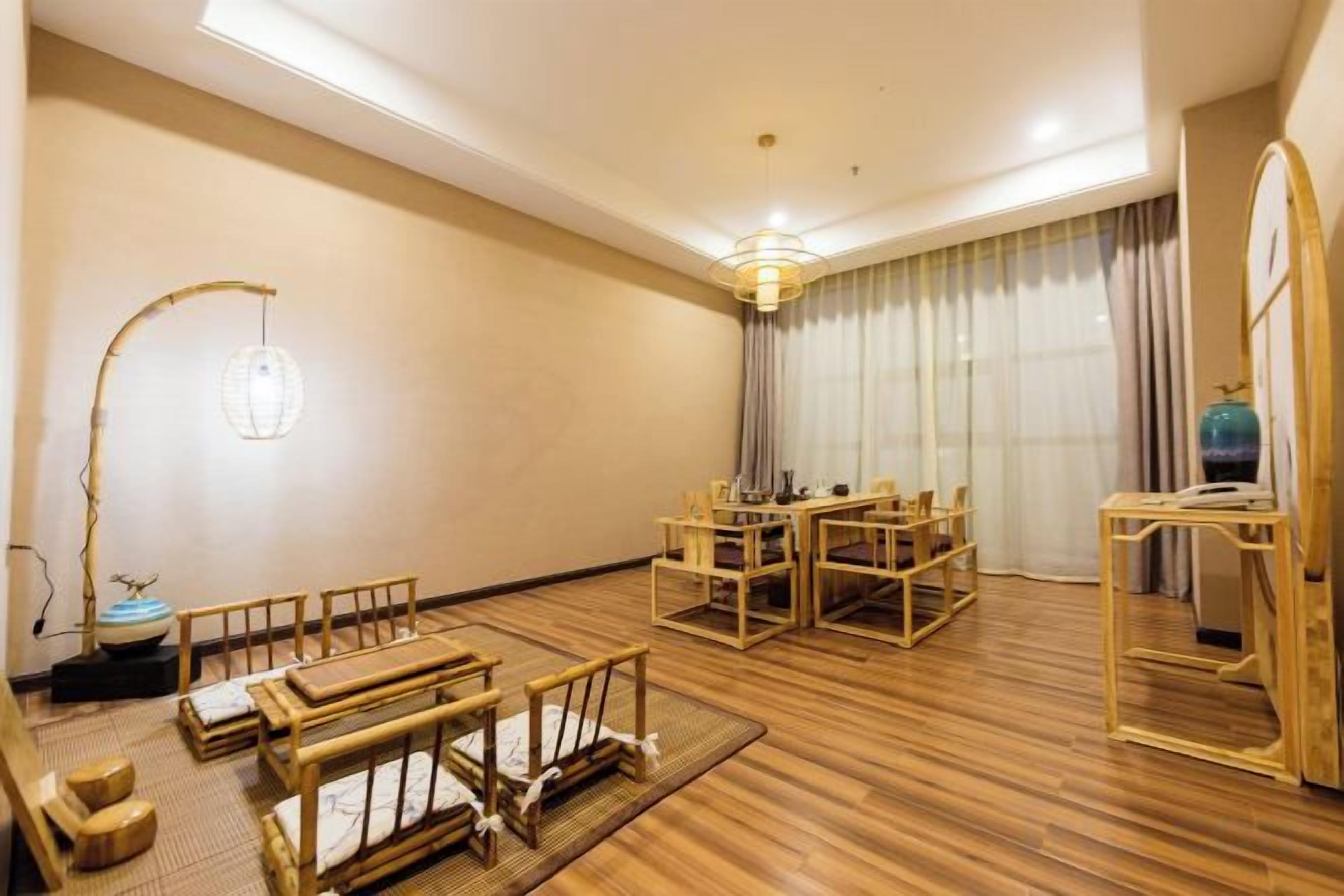 A room with a wooden floor, a dining table with chairs, a sofa, a lamp, and a mirror.