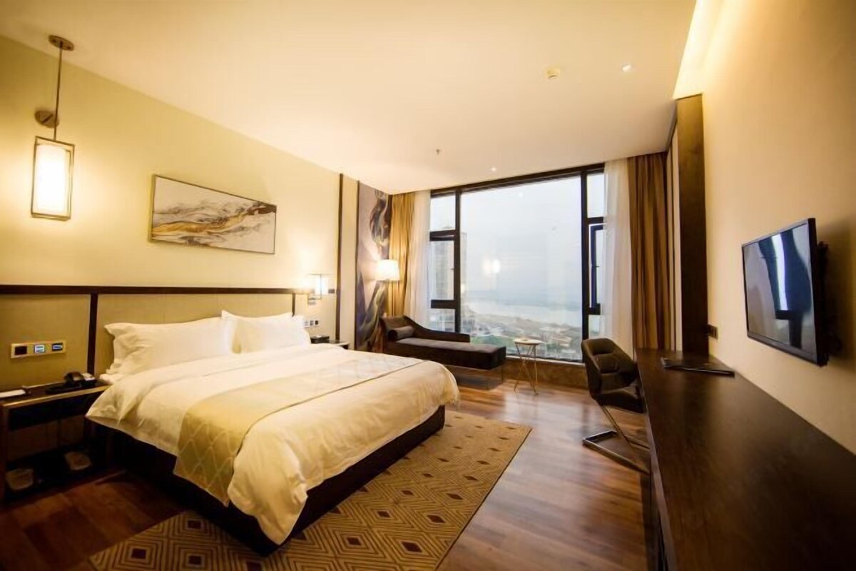 A hotel room with a large bed, a desk, a chair, a TV, and a city view.