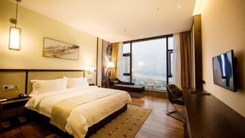 A hotel room with a large bed, a desk, a chair, a TV, and a city view.