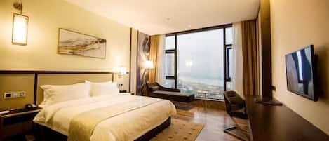 A hotel room with a large bed, a desk, a chair, a TV, and a city view.