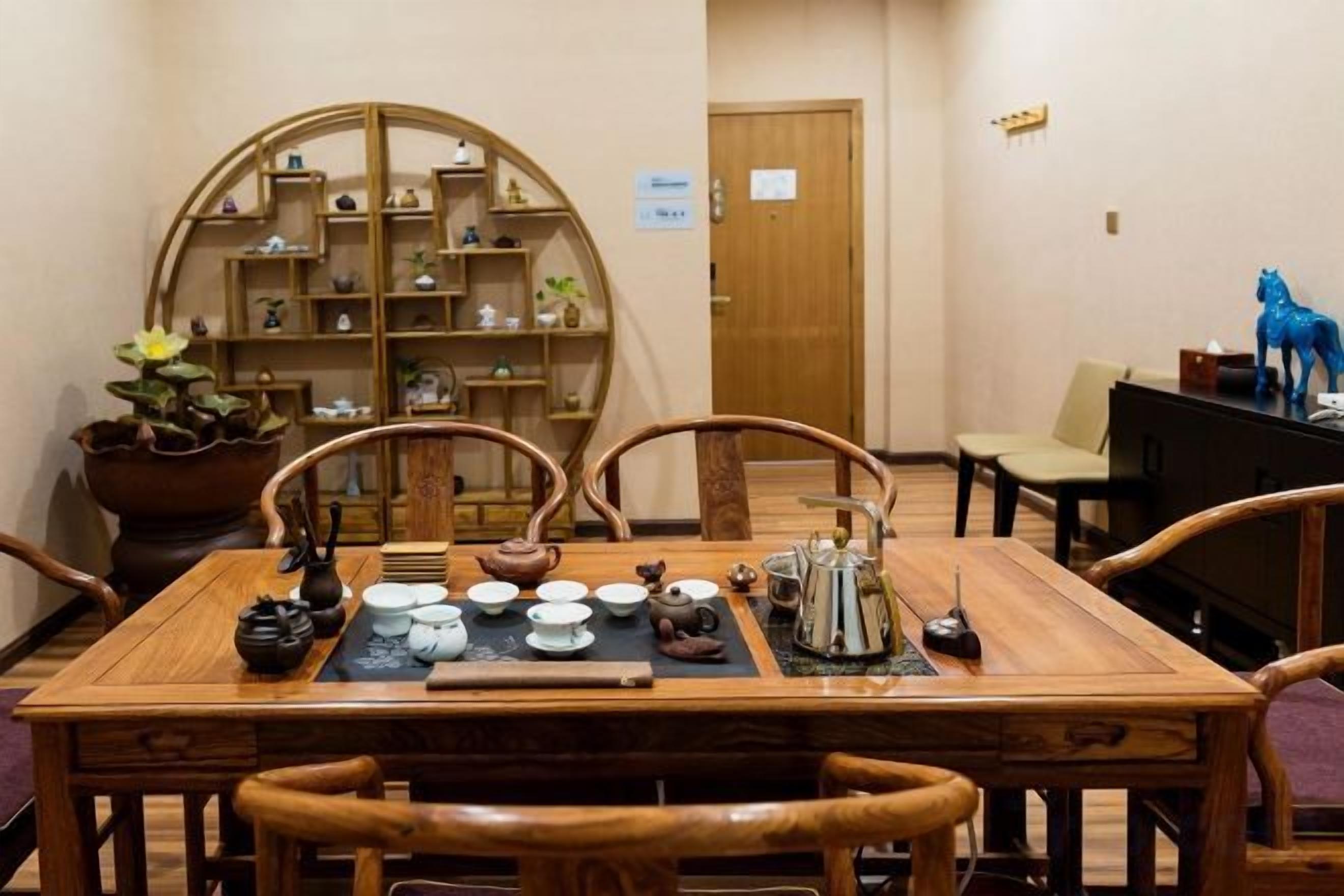 A wooden dining table with chairs, a tea set, and a bookshelf in the background.