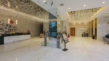 A hotel lobby with a reception desk, a glass elevator, and a modern interior design.