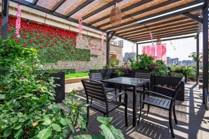 Un patio al aire libre con una mesa y sillas, rodeado de follaje y vistas a la ciudad.