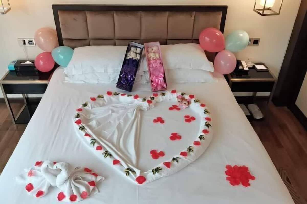 Una habitación de hotel con una cama, almohadas, una mesita de noche y una lámpara de pared.