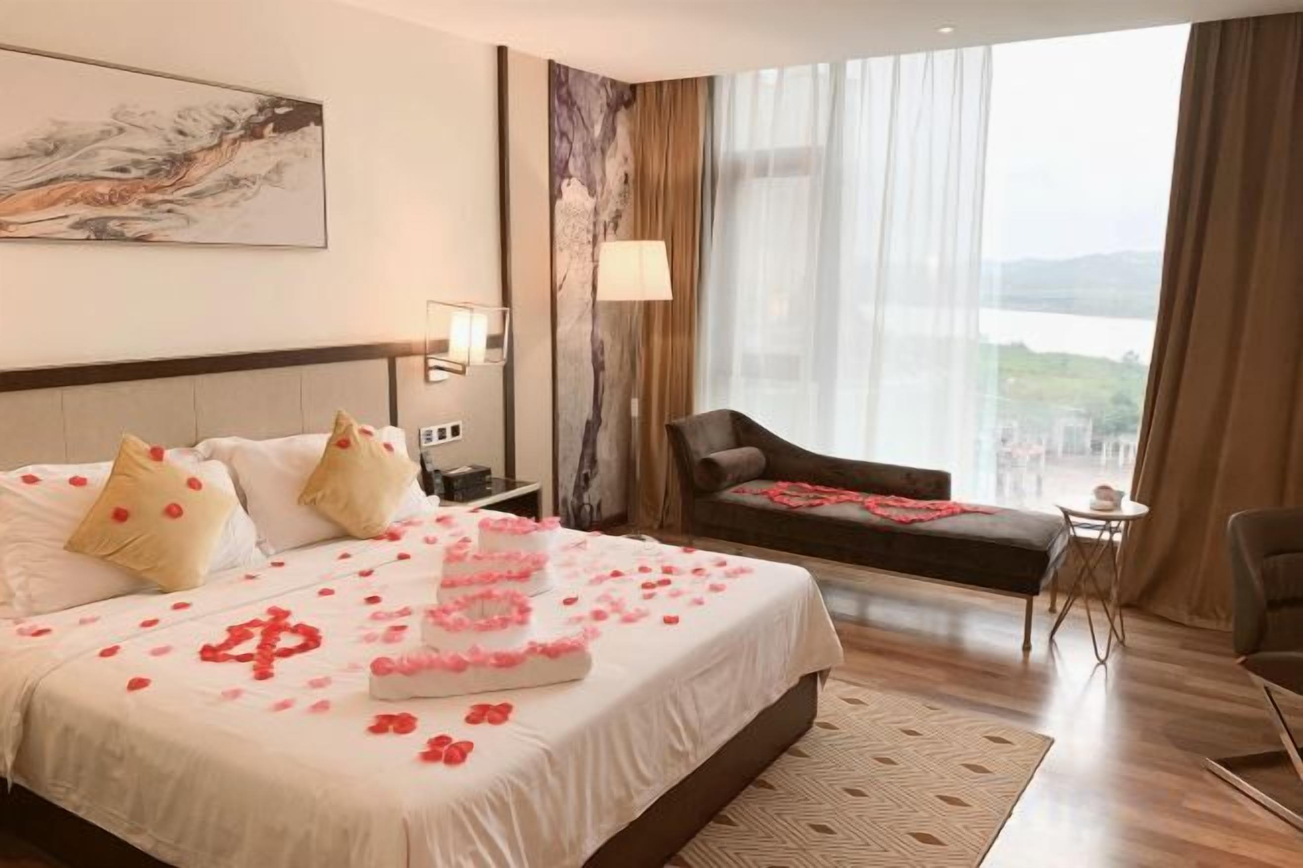 A hotel room with a large bed, a sitting area with a view, and a window with curtains.