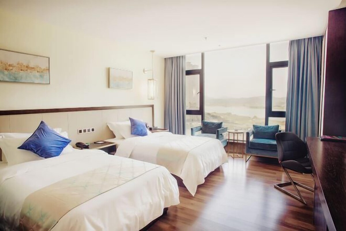 A hotel room with two beds, a desk, a chair, and a view of the beach.