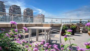 Terraço no telhado com mesa e cadeiras, rodeado por vasos de plantas e flores.