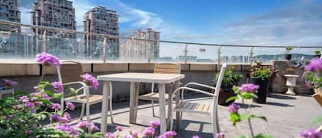 A rooftop terrace with a table and chairs, surrounded by potted plants and flowers.