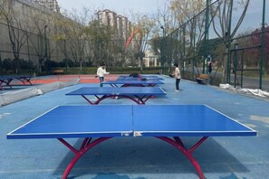 An outdoor table tennis court with multiple tables and a fence surrounding it.