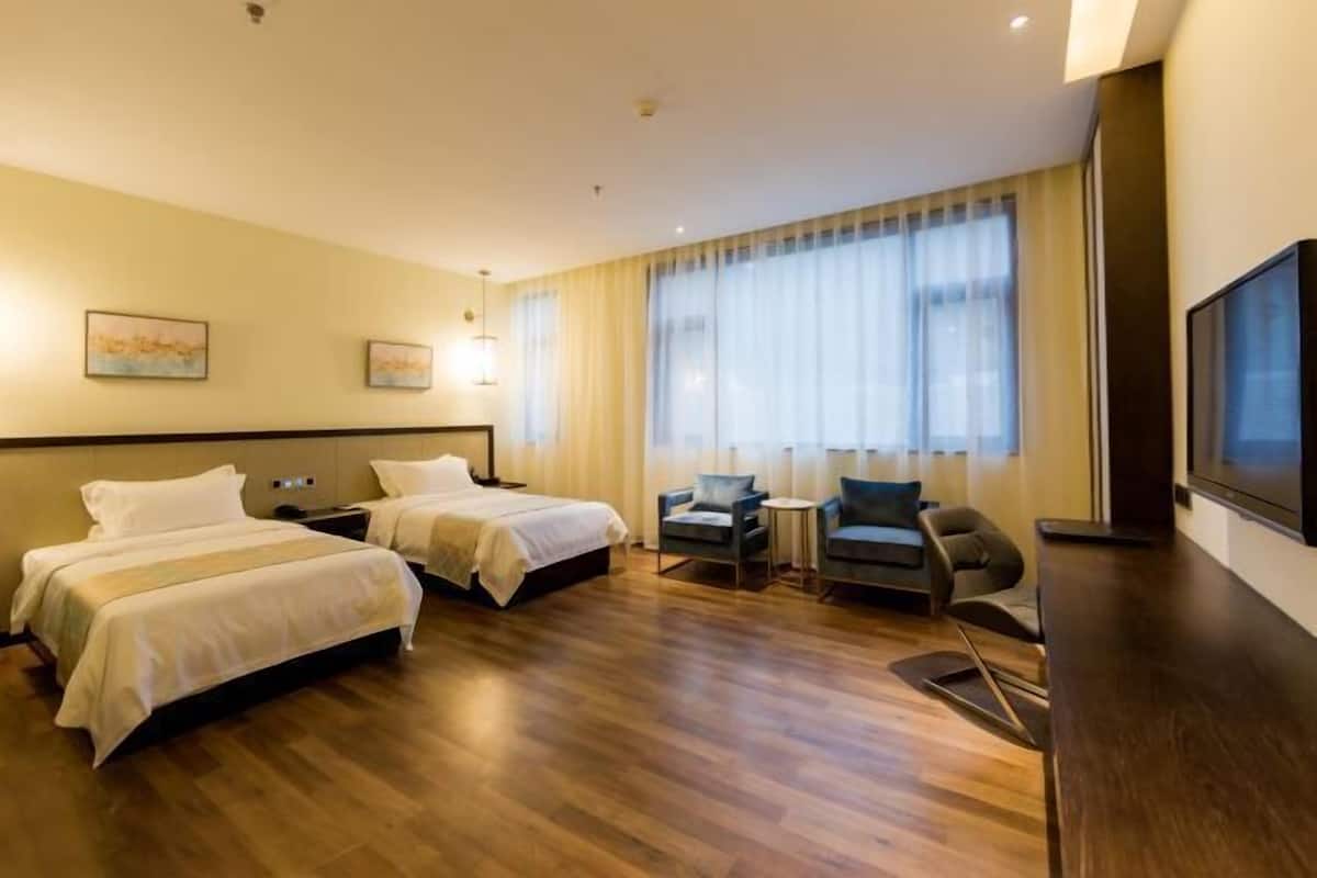 Habitación de hotel con dos camas, un escritorio, una silla, un televisor y un ventanal con cortinas.