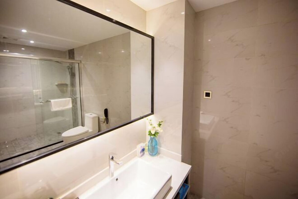 A modern bathroom with a large mirror, a white sink, and a glass shower enclosure.