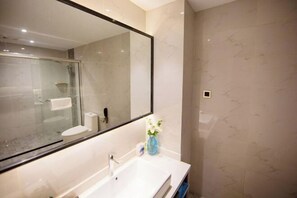 A modern bathroom with a large mirror, a white sink, and a glass shower enclosure. - Binjiang Celebrity Holiday Hotel (Nanbu County)