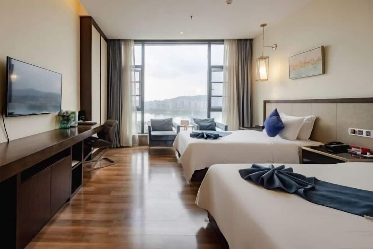 Una habitación de hotel con dos camas, un escritorio, un televisor y un ventanal con vistas.