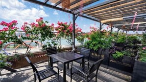 Un patio al aire libre con una mesa y sillas, rodeado de abundante vegetación y plantas en flor.