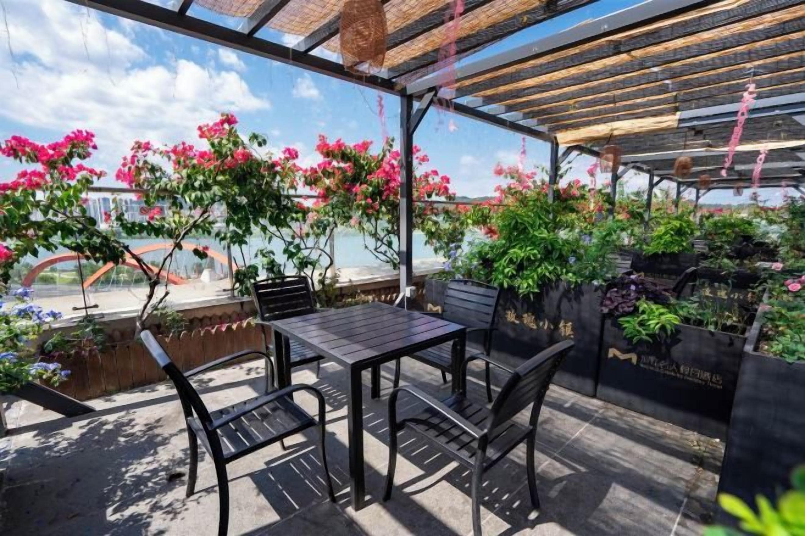 An outdoor patio with a table and chairs, surrounded by potted plants and flowers.