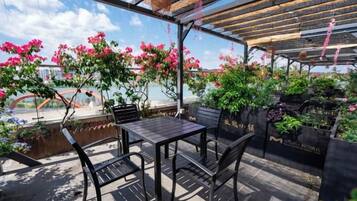 Eine Terrasse im Freien mit Tisch und Stühlen, umgeben von Blumentöpfen und Blumen.