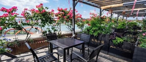 An outdoor patio with a table and chairs, surrounded by potted plants and flowers.