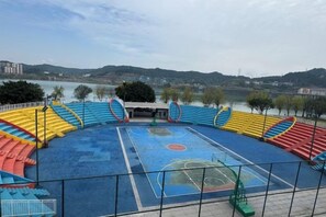 Una cancha de baloncesto al aire libre con vistas a un cuerpo de agua y colinas al fondo.
