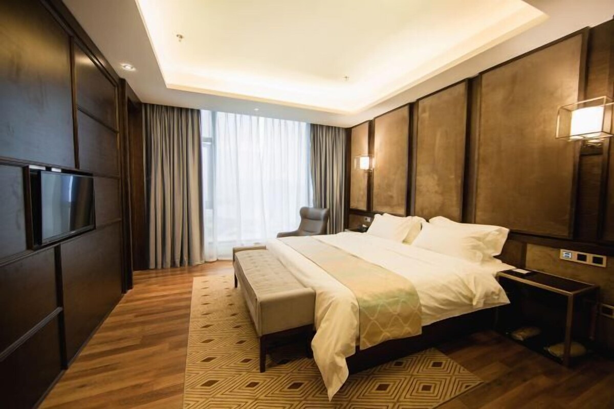 A modern hotel room with a large bed, a bench, a TV, and a bedside table.