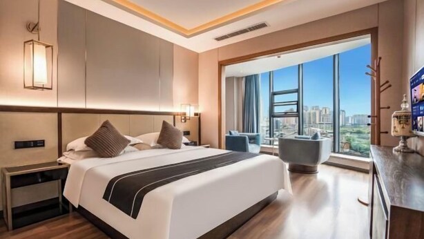 Una habitación de hotel moderna con una cama grande, una mesita de noche, un escritorio, una silla y un amplio ventanal con vistas a la ciudad.