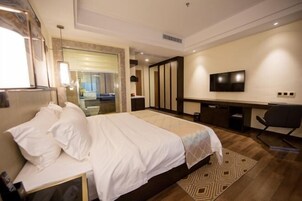 Habitación de hotel con una cama grande, un escritorio, una silla, un televisor y un baño visible a través de una puerta abierta.
