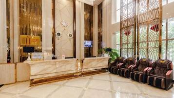 A hotel reception area with a marble counter, massage chairs, and a large window with decorative glass panels.