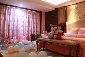 Une pièce avec un lit, une table décorée de ballons et un ours en peluche à l’effigie de Mickey Mouse.
