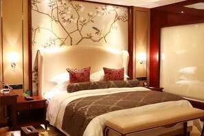 A hotel room with a large bed, a bedside table, a nightstand, and a wall with floral wallpaper.