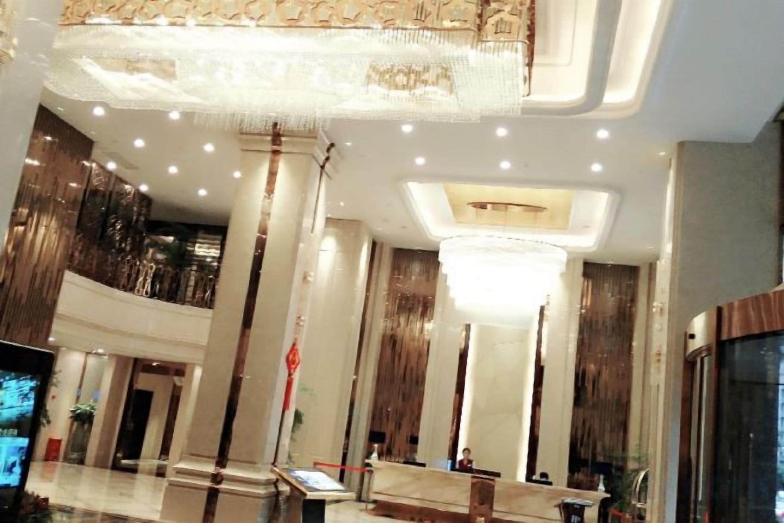 A hotel lobby with a high ceiling, chandeliers, and a reception desk.
