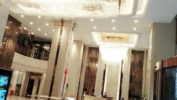 A hotel lobby with a high ceiling, chandeliers, and a reception desk.