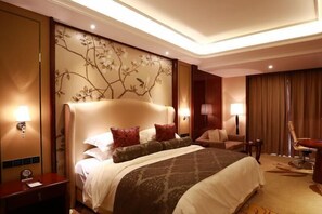 Une chambre d’hôtel avec un grand lit, un bureau, une chaise et un mur orné d’un motif floral.