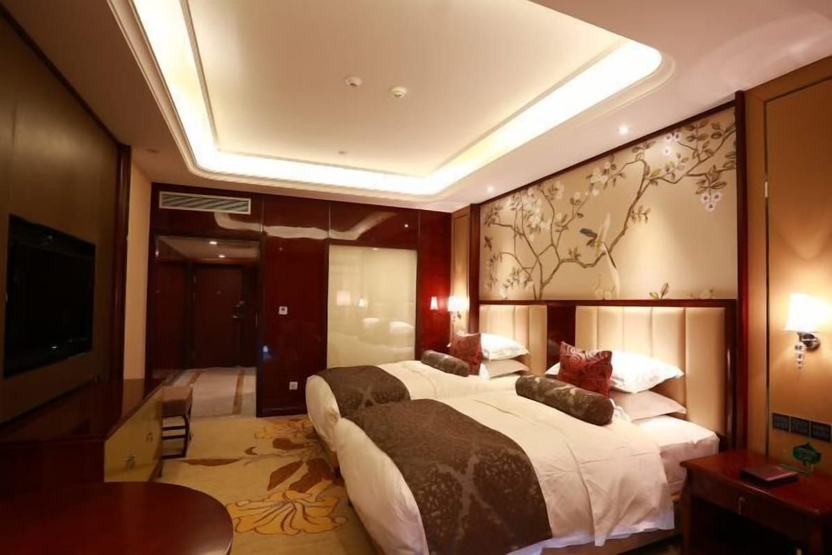 Une chambre d’hôtel avec deux lits, un grand téléviseur à écran plat, un mur décoratif et un plafond doté d’un éclairage encastré.