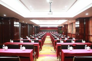 Un salón de conferencias con filas de mesas, cada una cubierta con un mantel rojo y botellas de agua.
