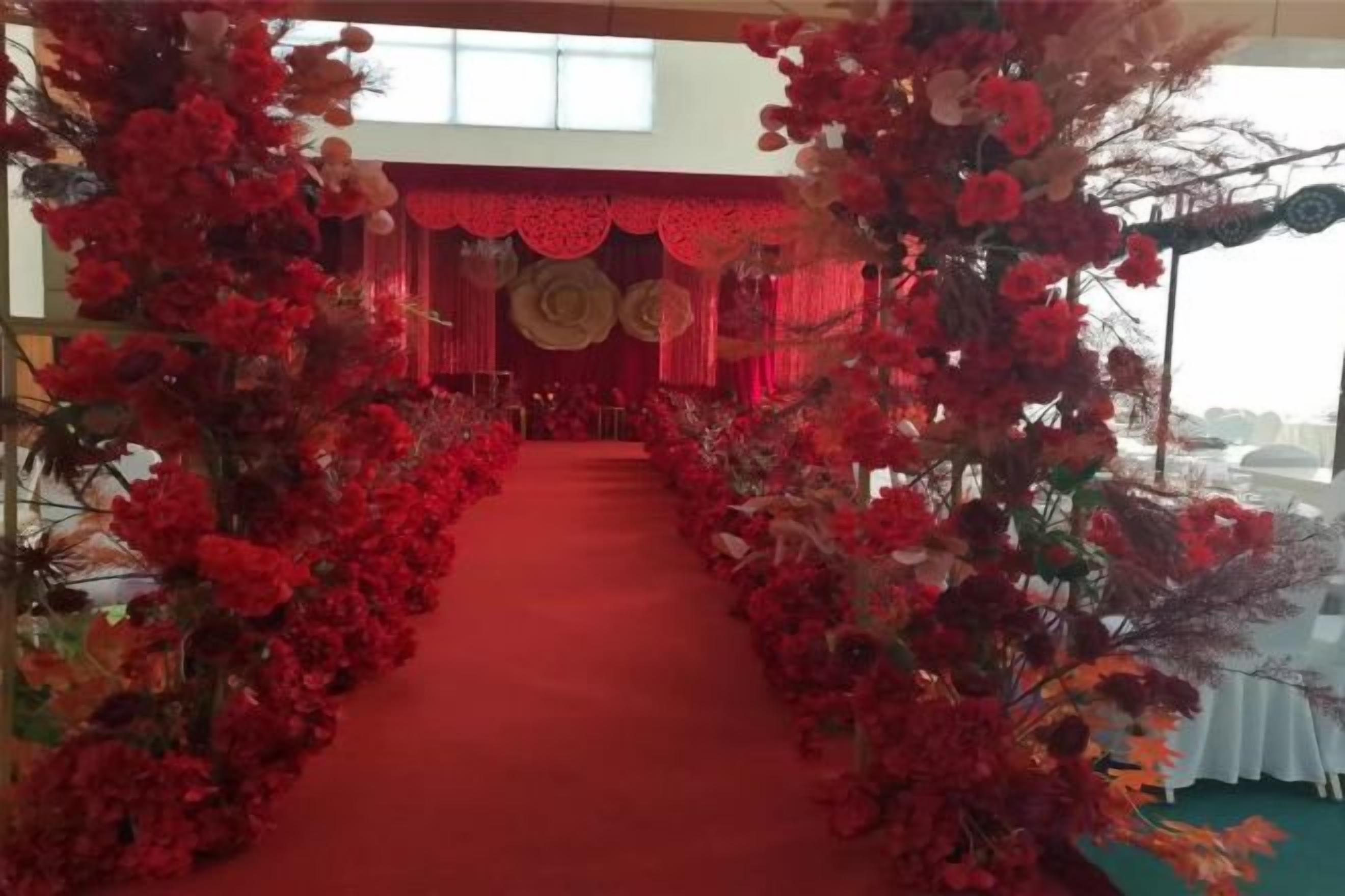 A red carpet aisle flanked by floral arrangements leading to a stage with a red backdrop.