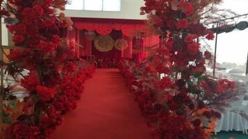 A red carpet aisle flanked by floral arrangements leading to a stage with a red backdrop.