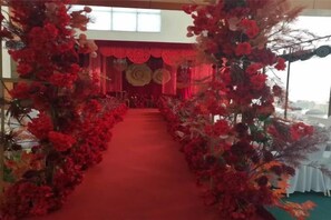 A red carpet aisle flanked by floral arrangements leading to a stage with a red backdrop. - Mingdu International Hotel (Bazhong)