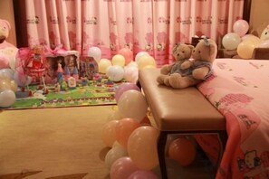 A room with a bed, a bench, and a play area with toys and balloons. - Mingdu International Hotel (Bazhong)
