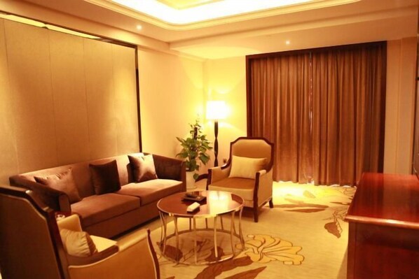 Une chambre d’hôtel avec un canapé marron, une table basse ronde, une chaise, une lampe et un rideau.